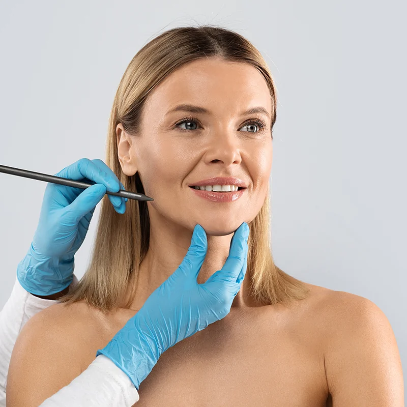 plastic surgeon drawing contours on mature woman's face during facelift consultation