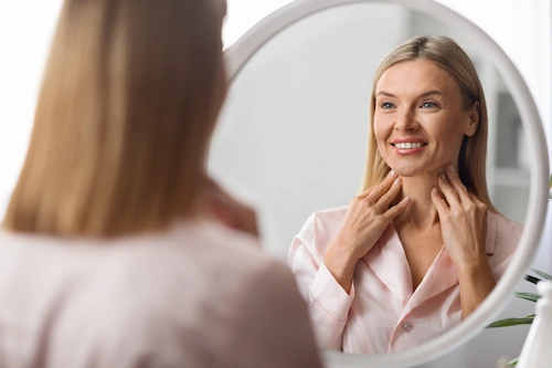 Happy woman looking in the mirror after a neck lift procedure